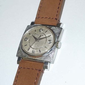 May include: A silver square-shaped watch with a brown leather band. The watch face has a silver background with black Roman numeral hour markers and black hands. There are four small diamonds around the watch face.