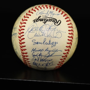 Op de afbeelding: Een witte honkbal met rode naden en talrijke blauwe handtekeningen, waaronder "Randy Myers" en "Sammy Sosa", op het oppervlak. De honkbal is een souvenir van de World Series van 1998.