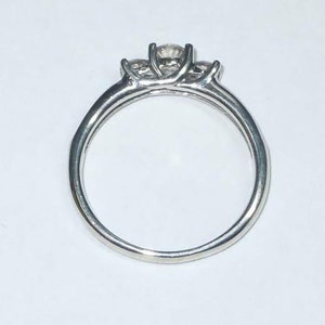 May include: A silver ring with three clear stones set in a prong setting.