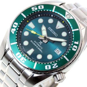 May include: A stainless steel Seiko automatic diver's watch with a teal dial and a green rotating bezel. The watch features white luminescent markers, a date window, and a silver band. The watch is water resistant to 200m.