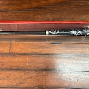May include: A black baseball bat with white accents and a silver band, displayed in a clear acrylic case with a red top. The bat features the Rawlings logo and the name "Darryl Strawberry" with the number "34/86".