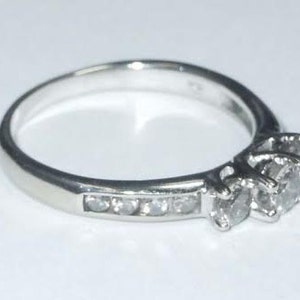 May include: A silver ring with three small diamonds set in a prong setting. The ring has a band of smaller diamonds.