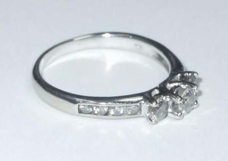 May include: A silver ring with three small diamonds set in a prong setting. The ring has a band of smaller diamonds.