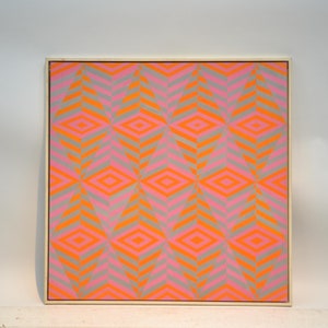 May include: Framed artwork with a geometric pattern. The design features repeating diamond shapes in vibrant orange and pink, set against a grey background. The artwork is encased in a light-coloured wooden frame.