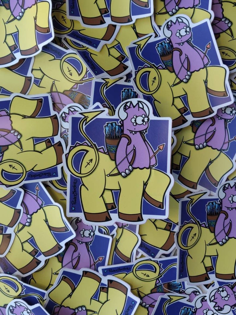 May include: A stack of colorful stickers featuring a purple monster with a yellow body and a bow and arrow. The monster has a tail and a single large eye. The stickers are on a blue background with a white border.