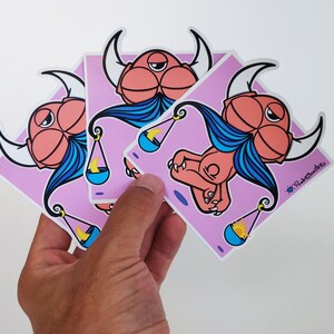 Peut inclure: Trois autocollants de dessin anim&eacute; rose et bleu repr&eacute;sentant un monstre avec des cornes et une barbe bleue tenant une balance avec une lune croissante et un soleil. Les autocollants sont sur un fond rose et portent le texte "PinkySmilers" dans le coin inf&eacute;rieur droit.