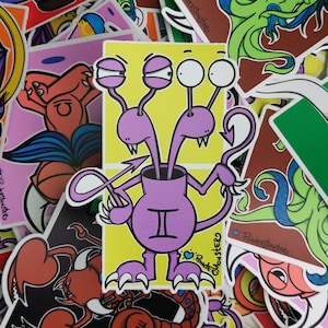 May include: A purple monster sticker with three eyes, two arms, and a tail. The monster is wearing a purple shirt with the astrological symbol for Gemini on it. The sticker is on a yellow background and has the text "Powder Monsters" on it.