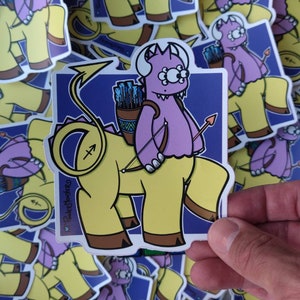 May include: A sticker featuring a cartoon illustration of a purple monster riding a yellow centaur. The monster has three eyes and is holding a bow and arrow. The centaur has a yellow body, a horse's head and legs, and a human torso. The sticker has a blue background with a white border and the text "Pocket Monster" in the bottom left corner.
