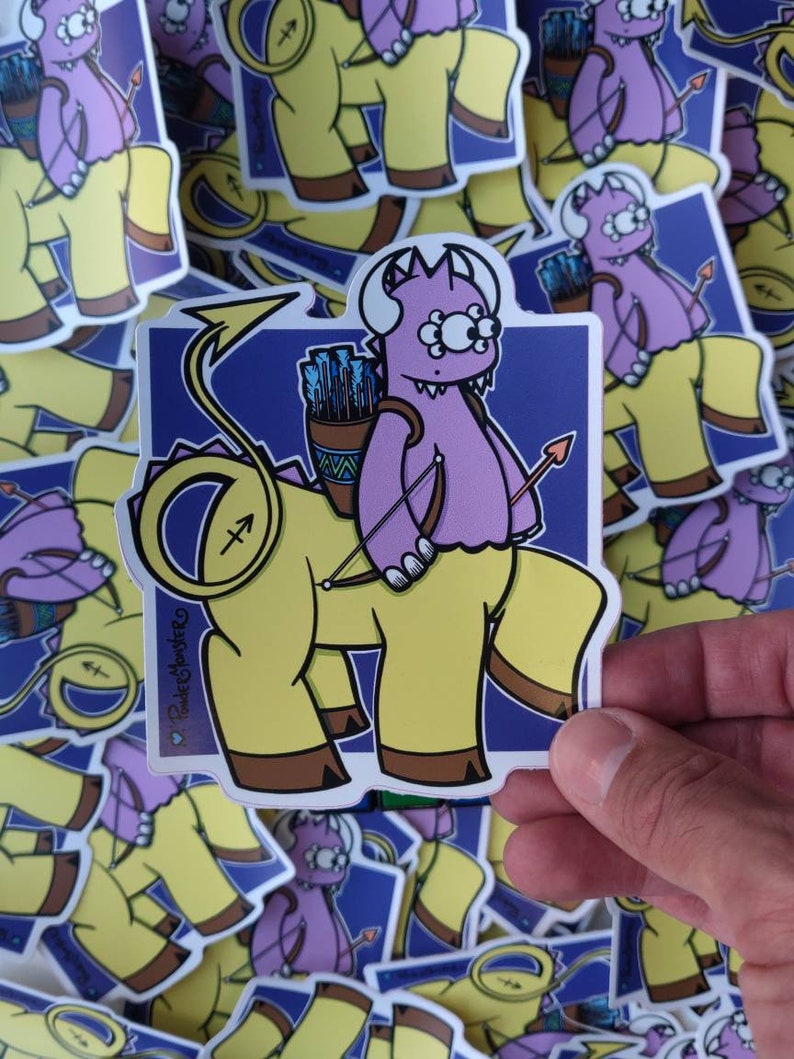 May include: A sticker featuring a cartoon illustration of a purple monster riding a yellow centaur. The monster has three eyes and is holding a bow and arrow. The centaur has a yellow body, a horse's head and legs, and a human torso. The sticker has a blue background with a white border and the text "Pocket Monster" in the bottom left corner.