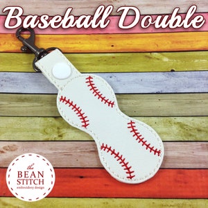 May include: White leather keychain with a baseball design. The keychain has a red stitching detail and a silver metal clasp. The keychain is on a wooden background with colorful stripes.