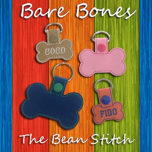 May include: Four dog bone-shaped keyrings with different colours and personalised names. The keyrings are made of leather and have a stitched edge. The names on the keyrings are "Coco", "Fido", and two blank keyrings. The keyrings are displayed on a wooden background.
