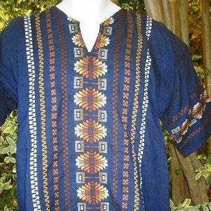 May include: A dark blue tunic with a geometric pattern in shades of brown, white, and yellow. The tunic has a V-neck and short sleeves.