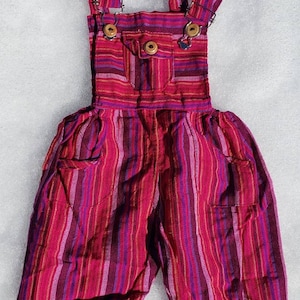 Puede incluir: Pantal&oacute;n vaquero rojo y morado a rayas con un peque&ntilde;o bolsillo en la parte delantera. El pantal&oacute;n vaquero tiene tirantes ajustables con botones de madera.