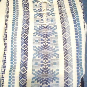 May include: White tunic with blue and white geometric patterns and a white lace-up neckline.