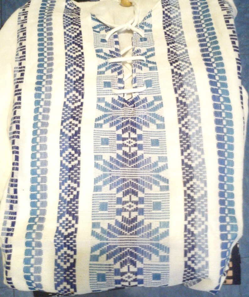 May include: White tunic with blue and white geometric patterns and a white lace-up neckline.