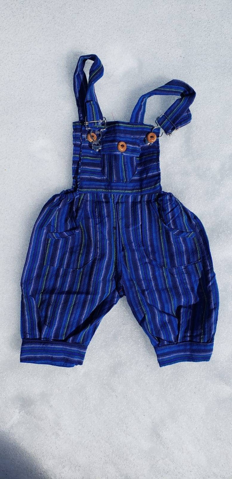 Puede incluir: Pantal&oacute;n vaquero de beb&eacute; a rayas azules y blancas con dos botones de madera. El pantal&oacute;n tiene dos bolsillos en la parte delantera.