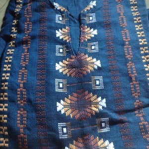May include: A blue cotton shirt with a geometric pattern in brown, white, and gold. The shirt has a v-neck and is folded in half.