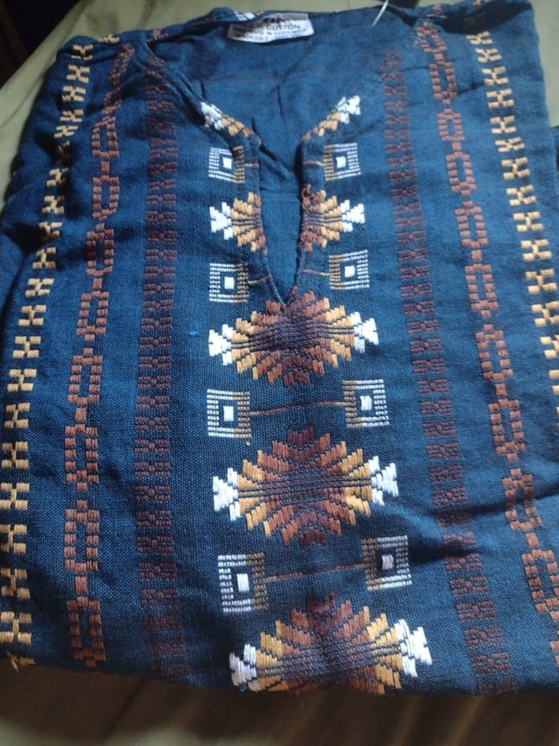 May include: A blue cotton shirt with a geometric pattern in brown, white, and gold. The shirt has a v-neck and is folded in half.