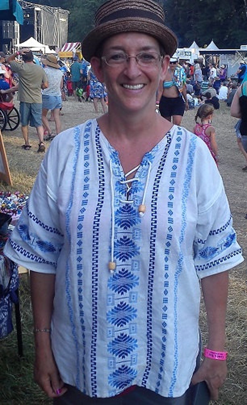 May include: A white embroidered blouse with blue and white geometric patterns. The blouse has a V-neck and a drawstring closure at the neckline. The blouse is made of a lightweight fabric and has a relaxed fit.
