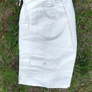May include: A pair of solid eggshell white linen shorts with a single buttoned pocket on the front.