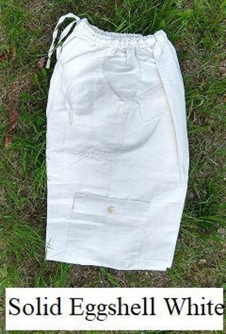 May include: A pair of solid eggshell white linen shorts with a single buttoned pocket on the front.