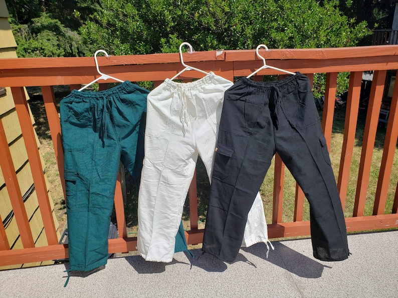 May include: Three pairs of pants hanging on a wooden railing. The pants are green, white, and black.