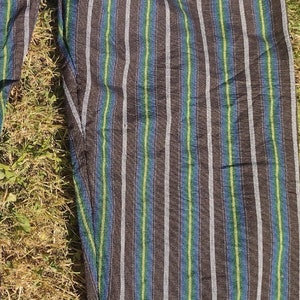 Puede incluir: Pantal&oacute;n negro a rayas con finas rayas blancas, verdes y azules. El pantal&oacute;n tiene un bolsillo en el lado derecho.