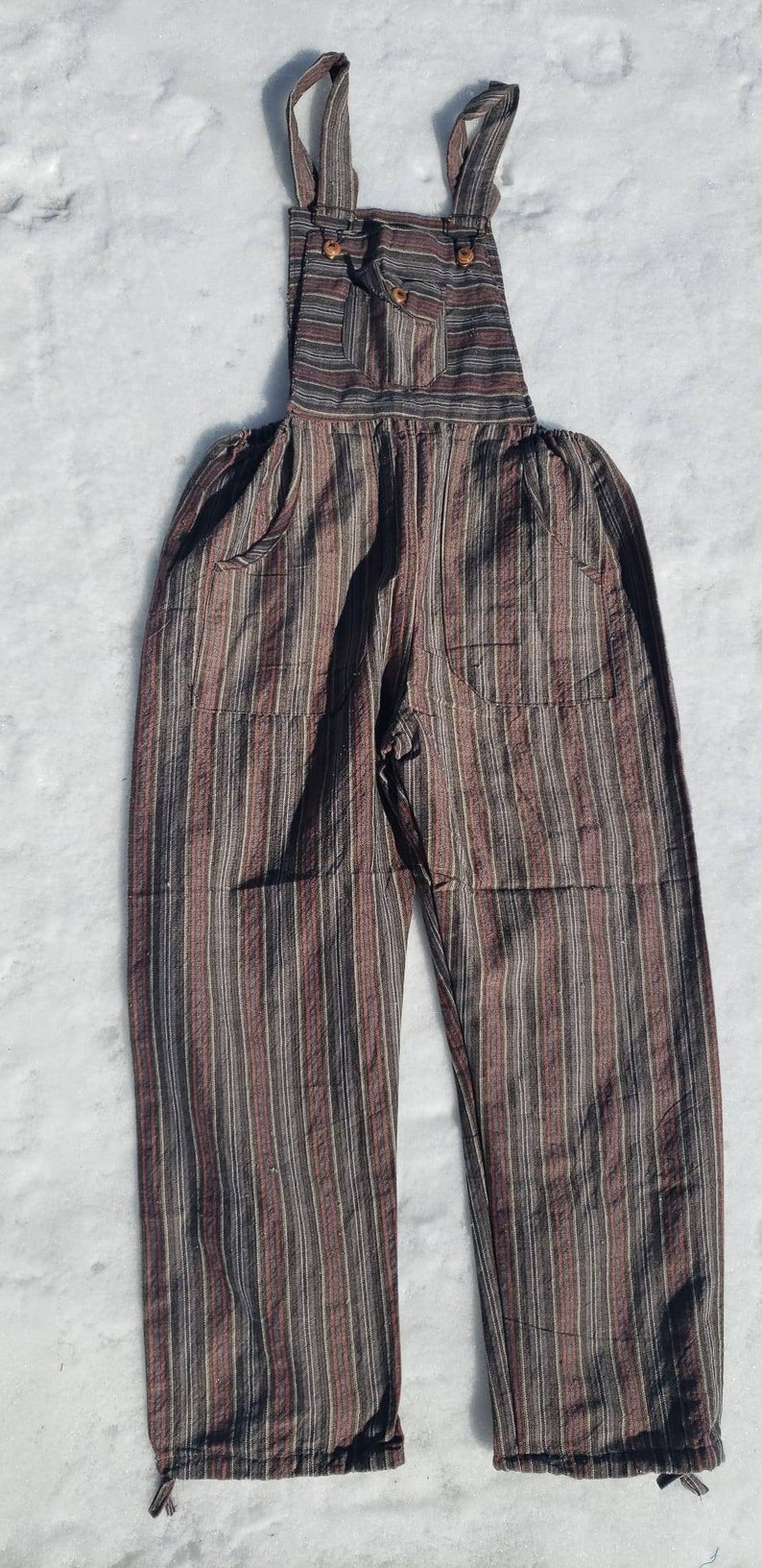 Puede incluir: Pantal&oacute;n vaquero de rayas marrones y negras de algod&oacute;n con tirantes ajustables y bolsillos.