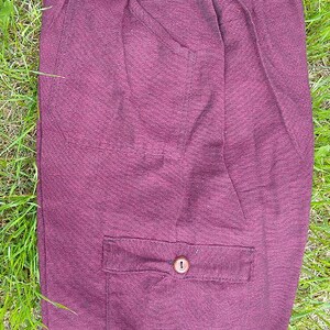 May include: A solid burgundy pair of pants with a drawstring waist and a single button pocket on the front.