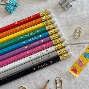 May include: A set of ten rainbow colored pencils with a gold eraser and a gold trim. Each pencil has the name "PHOEBE" written on it in gold lettering with a gold heart symbol.