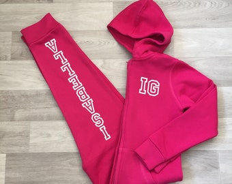 May include: A pink hooded jumpsuit with white lettering on the sleeves and chest. The lettering on the sleeves says "1987" and the lettering on the chest says "IG".