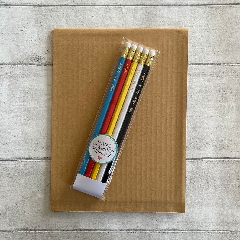May include: A set of six hand-stamped pencils in a clear plastic bag. The pencils are black, white, yellow, and blue. The pencils are stamped with the phrases "How You Don't?", "Pivot", "Oh My God", and "We Were On A Break". The pencils are packaged with a round sticker that says "Hand Stamped Pencils".