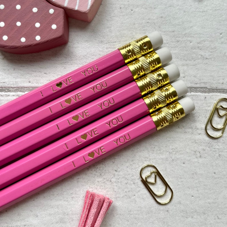 May include: Five pink pencils with gold accents and white erasers. Each pencil has the words "I LOVE YOU" printed on it with a small gold heart.