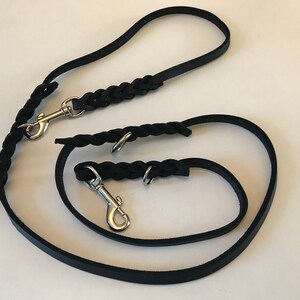 May include: Two black leather dog leashes with silver clips. The leashes are braided and have a flat strap.