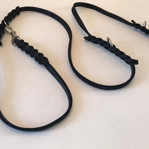 May include: Two black leather dog leashes with braided detailing and silver metal clasps.