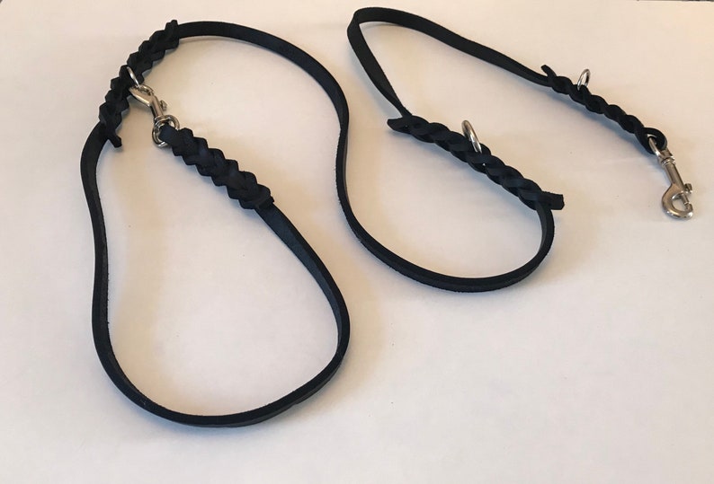 May include: Two black leather dog leashes with braided detailing and silver metal clasps.