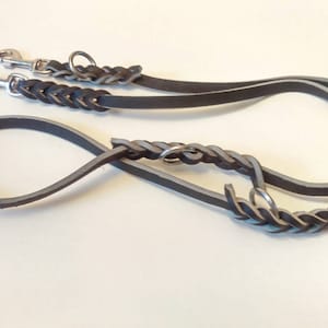 May include: A black leather dog leash with a braided design and two silver clips. The leash is designed for two dogs.