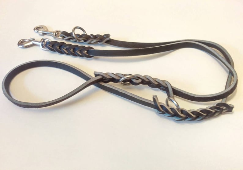 May include: A black leather dog leash with a braided design and two silver clips. The leash is designed for two dogs.