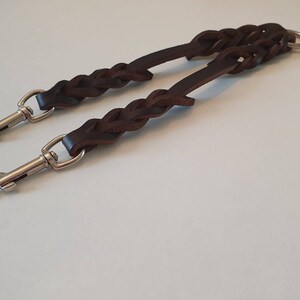 May include: A brown leather dog lead with two metal clips and a metal ring. The lead is braided and has a double-ended design.