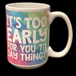 May include: White ceramic coffee mug with a colorful geometric pattern and the text "It's too early for you to say things".