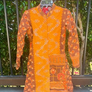 May include: A long-sleeved, quilted jacket with a button-up front. The jacket is made of a patchwork of fabrics in shades of brown, orange, and red. The fabric features a floral pattern and geometric designs.