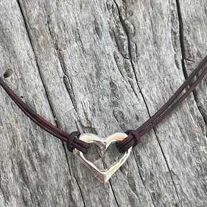 May include: A brown leather cord necklace with a silver heart pendant. The heart has a cutout design and is slightly textured.