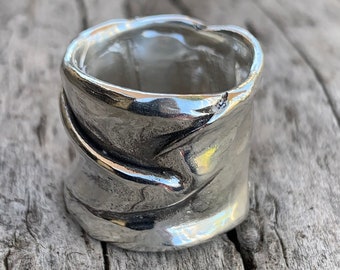 May include: A silver ring with a textured, organic design. The ring is wide and has a rounded shape.