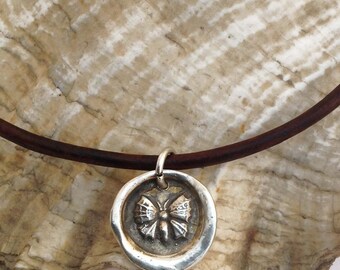 May include: A silver necklace with a leather cord and a round pendant featuring a detailed butterfly design.
