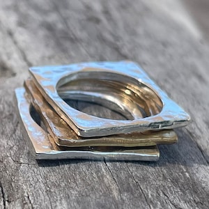 Puede incluir: Pila de cuatro anillos cuadrados de plata y oro con textura martillada.