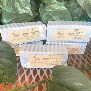 May include: Four bars of gray foot scrub soap with a goat and the text "THE FOOT SCRUB soap + pumice a girl & a goat scrub on damp feet, keep dry between uses" on each bar.