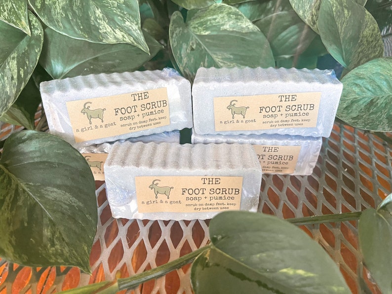 Może przedstawiać: Cztery szare kostki mydła do peelingu st&oacute;p z kozą i tekstem "THE FOOT SCRUB soap + pumice a girl & a goat scrub on damp feet, keep dry between uses" na każdej kostce.