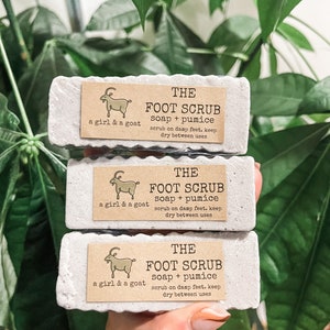 Może przedstawiać: Trzy białe kostki mydła z ilustracją kozy i tekstem "THE FOOT SCRUB soap + pumice scrub on damp feet. keep dry between uses" na każdej kostce.