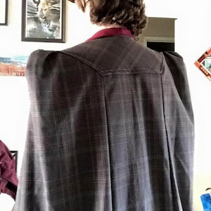 Op de afbeelding: Een geruite jas met een bordeauxrode kraag en opgeblazen schouders. De jas is gemaakt van een zachte, comfortabele stof en heeft een klassiek, tijdloos ontwerp.