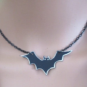 May include: A black bat pendant necklace with a silver chain. The bat is made of metal and has a slightly textured surface.